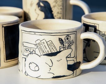 May include: A white ceramic mug with a black and white illustration of a cat sleeping on a stack of books. The mug has a black rim and handle. The illustration also includes a flower and a plant.