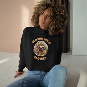 Cropped hoodie in black, Relax in style with our Sloth Rule Slowly Crop Hoodie, boasting a relaxed fit, dropped shoulders, and raw bottom hem for a laid-back look.