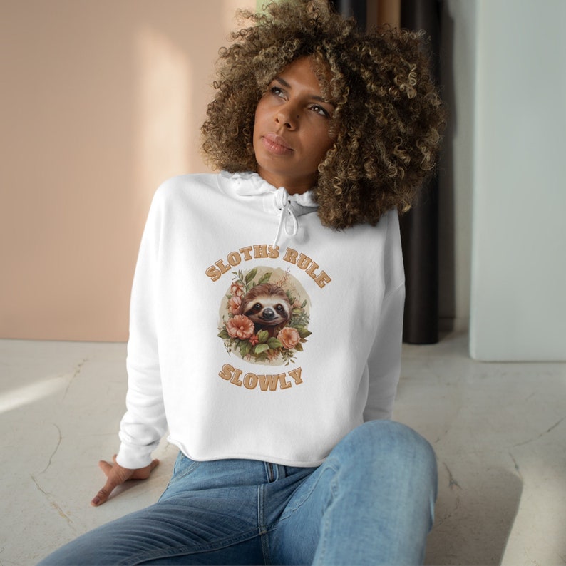 Cropped hoodie in white with funny sloth design. Embrace the sloth life in style with our black Sloth Rule Slowly Crop Hoodie – perfect for cozy evenings at home or casual outings with friends.