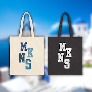 Puede incluir: Dos bolsas de tela con la palabra "MNKS" impresa en ellas. Una bolsa es blanca con letras azules y la otra es negra con letras blancas.