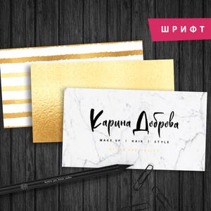 May include: A white marble business card with black text that reads "Karina Dobrova" and "Make Up | Hair | Style | Style Specialist". The card is on a wooden surface with a gold and white striped card and a gold card behind it.