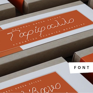 May include: Close-up of two brown cardboard boxes with orange labels. The labels have white text that reads "NATURAL GREEK SPICES" and "Χαρίμα" in cursive. The text on the bottom label reads "ΑΥΘΕΝΤΙΚΑ ΕΛΛΗΝΙΚΑ ΜΠΑΧΑΡΙΚΑ".