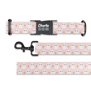 May include: Pink dog collar and leash with a pattern of white ghosts and orange pumpkins. The collar has a black buckle with the name "Charlie" and phone number "123-456-7890" printed on it.