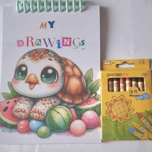 May include: A drawing pad with a spiral binding, featuring the words "MY DRAWINGS" and a cartoon turtle illustration. Beside it is a yellow box of crayons with a sunflower design and the word "Crayons".