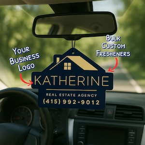 May include: A navy blue car air freshener with a gold house design and the name "KATHERINE" in gold lettering. The text "REAL ESTATE AGENCY" and a phone number are also displayed. The words "Bulk Custom Freshners" and "Your Business Logo" are also visible.
