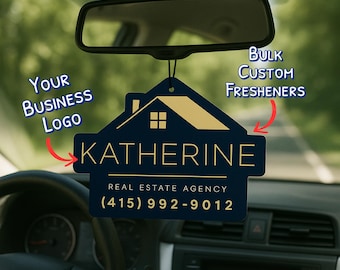 May include: A navy blue car air freshener with a gold house design and the name "KATHERINE" in gold lettering. The text "REAL ESTATE AGENCY" and a phone number are also displayed. The words "Bulk Custom Freshners" and "Your Business Logo" are also visible.