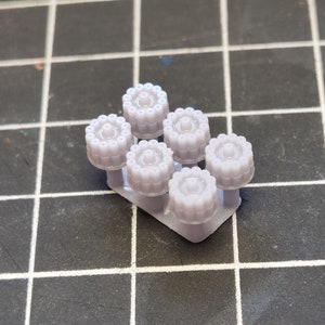 May include: A set of six gray plastic model wheels with a detailed design. The wheels are arranged in a row on a gray plastic sprue.