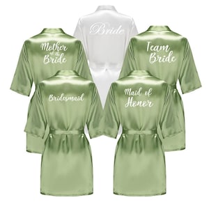 May include: A collection of satin robes in white and green. The white robe is labeled "Bride", while the green robes are labeled "Mother of the Bride", "Bridesmaid", "Maid of Honor", and "Team Bride". Each robe has a matching belt.