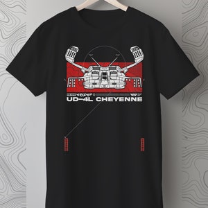 Op de afbeelding: Zwart T-shirt met een witte afbeelding van een futuristisch ruimteschip met de tekst "UD-4L CHEYENNE" eronder. De afbeelding is op een rode achtergrond met witte accenten. Het T-shirt heeft een wit label met de tekst "2048 DARK SHOP" in de rechterbenedenhoek.