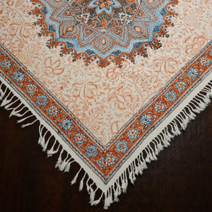 Könnte beinhalten: Eine weiße Tischdecke mit einem blauen und orangefarbenen Blumenmuster und einem Fransenrand. Die Tischdecke hat ein zentrales Medaillon-Design mit komplizierten Details.