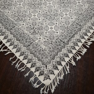 May include: A white tablecloth with a black and white paisley pattern and fringe trim. The tablecloth is made of cotton and is ideal for a table setting.