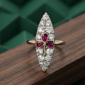 Può includere: Un anello a forma di marquise con un motivo centrale a trifoglio composto da tre rubini rossi taglio a pera incastonati in oro, circondato da un gruppo di diamanti bianchi taglio brillante montati su metallo argentato e fascia in oro.