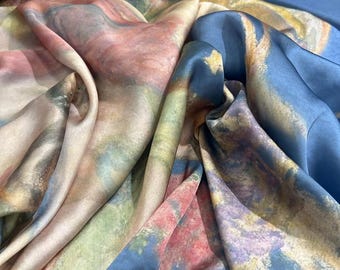 May include: A close-up of a flowing fabric with a watercolor-like design. The fabric features a blend of colors, including blues, pinks, greens, and yellows. The material appears to be soft and silky, with visible folds and creases.
