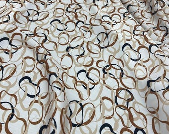 Puede incluir: Tela blanca con un patrón repetitivo de formas abstractas e interconectadas en tonos marrón, beige y negro. La tela está doblada, creando sombras y profundidad, y es adecuada para ropa o decoración del hogar.
