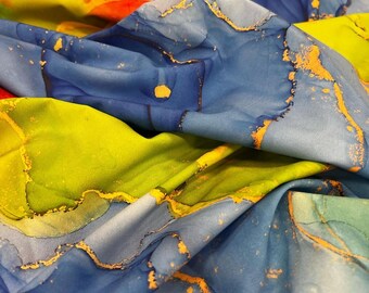 May include: Close-up of a fabric with an abstract design. The fabric features flowing patterns in shades of blue, yellow, and red, with gold accents. The fabric is folded, creating shadows and depth, highlighting the texture and color variations.