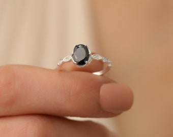 Könnte beinhalten: Ein silberner Ring mit einem schwarzen ovalen Edelstein, der von kleineren klaren Edelsteinen umgeben ist.
