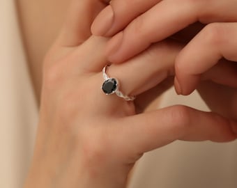 Könnte beinhalten: Ein silberner Ring mit einem schwarzen ovalen Edelstein, der in einem zarten, blattartigen Band gefasst ist.
