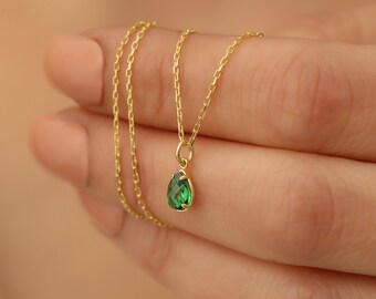 May include: A delicate gold chain necklace with a small pear-shaped green gemstone pendant.