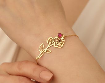 May include: A gold rose bracelet with a pink gemstone. The rose is cut out and the bracelet is delicate.