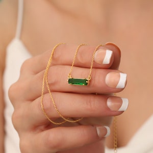 Puede incluir: Un collar de cadena dorada con un colgante rectangular verde.