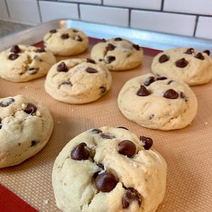 Op de afbeelding: Een close-up van een bakplaat met vers gebakken chocoladekoekjes. De koekjes zijn goudbruin en hebben een licht knapperige buitenkant. Sommige koekjes hebben een snufje zeezout erop.