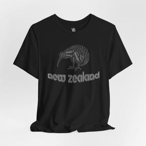Puede incluir: Camiseta negra con un gr&aacute;fico blanco de un kiwi hecho de palabras. El texto "new zealand" est&aacute; impreso debajo del p&aacute;jaro.
