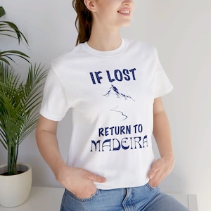 Puede incluir: Camiseta blanca con el texto azul marino "IF LOST RETURN TO MADEIRA". El diseño incluye un gráfico de montaña y un camino sinuoso. La camiseta tiene cuello redondo y mangas cortas.