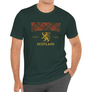 Puede incluir: Camiseta verde oscuro con la palabra "EDINBURGH" en un dise&ntilde;o de cuadros rojos. Debajo, un emblema de le&oacute;n dorado y la palabra "SCOTLAND" en blanco. Cuello redondo y mangas cortas.