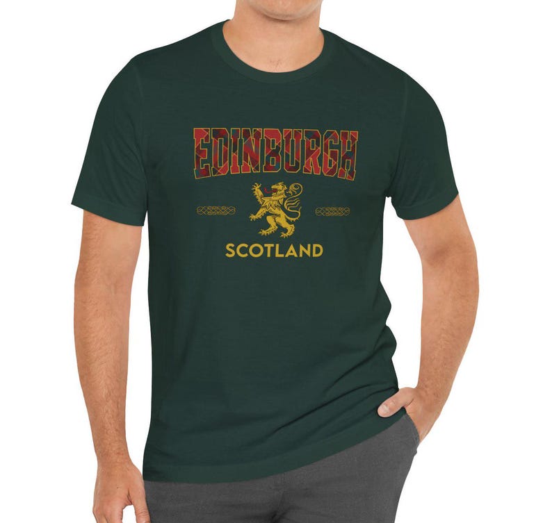 Puede incluir: Camiseta verde oscuro con la palabra "EDINBURGH" en un dise&ntilde;o de cuadros rojos. Debajo, un emblema de le&oacute;n dorado y la palabra "SCOTLAND" en blanco. Cuello redondo y mangas cortas.
