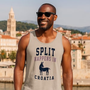 Può includere: Una canotta grigio chiaro con la scritta "SPLIT HAPPENS IN CROATIA" in blu navy e viola. Una grafica di asino blu scuro è sotto il testo. La persona indossa occhiali da sole neri e sorride.