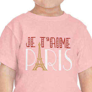 A todder wearing a pink tshirt that says "Je T'aime Paris". The A in "Paris" is replaced with a graphic of the Eiffel Tower.