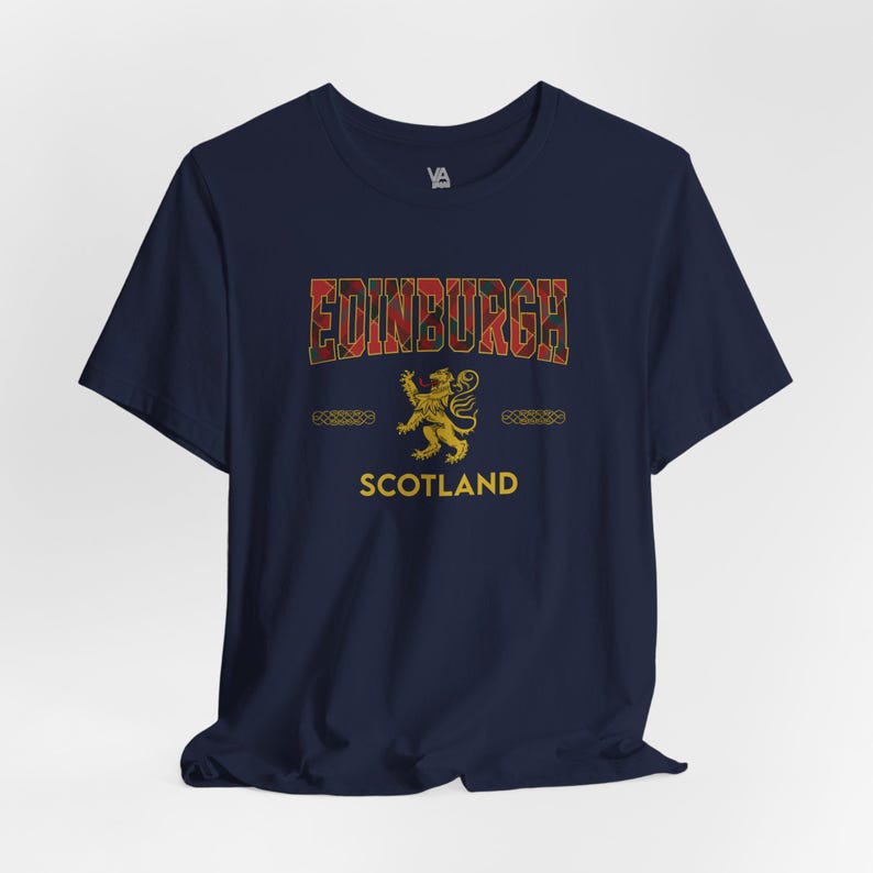 Puede incluir: Camiseta azul marino con la palabra "EDINBURGH" en un dise&ntilde;o escoc&eacute;s. Un emblema de le&oacute;n dorado y la palabra "SCOTLAND" est&aacute;n debajo. La camiseta tiene mangas cortas y cuello redondo.