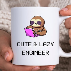 Könnte beinhalten: Eine weiße Keramiktasse mit einem Cartoon-Faultier, das einen rosa Laptop hält. Die Tasse trägt den Text "Cute & Lazy Engineer" in Schwarz.