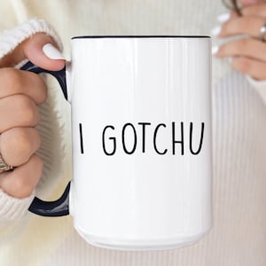 May include: White ceramic mug with a black rim and handle. The mug has the text "I GOTCHU" printed in black on the front.