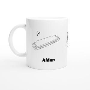 Puede incluir: Taza de cerámica blanca con un contorno negro de una armónica y notas musicales. La taza tiene el nombre "Aidan" impreso en la parte delantera.