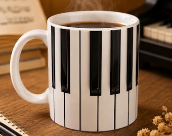 May include: A white ceramic mug featuring a black and white piano keyboard pattern wrapped around the exterior. The mug is filled with a dark brown liquid, and a thin wisp of steam rises from the top, indicating a hot beverage inside the vessel.