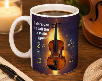 May include: A white ceramic mug featuring a dark purple and orange galaxy background with a brown string instrument in the center. The text reads, I dare you to call this a Violin again! Gold musical notes are scattered around the instrument.