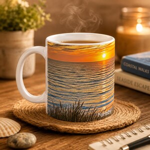 Op de afbeelding: Witte keramische mok met een zonsondergang boven de oceaan. De mok heeft een wit handvat en bevat een warme drank. Het woord "Formby" staat op de mok.