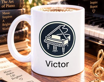 May include: A white ceramic mug featuring a circular graphic of a grand piano in black and cream colors. The name Victor is printed in black text below the graphic. The mug is filled with a hot beverage with visible steam rising from the top.