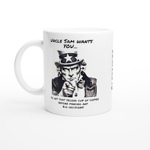 Può includere: Una tazza da caffè in ceramica bianca con un'illustrazione in bianco e nero di zio Sam che punta verso lo spettatore. Il testo sulla tazza recita "Uncle Sam Wants You... To get that second cup of coffee before making any big decisions!"