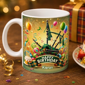 May include: A white ceramic mug featuring a colorful birthday design with bagpipes, balloons, streamers, and a small cake. A green banner across the center displays the text Happy Birthday Kieran in white lettering against a gold and green background.
