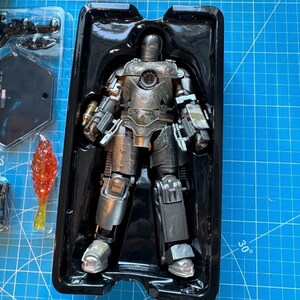 Może przedstawiać: Srebrna figurka Iron Mana w czarnym plastikowym etui. Figurka ma szczeg&oacute;łowy, zniszczony w walce wygląd z widocznymi nitami i liniami paneli. Akcesoria obejmują efekt płomienia i podstawkę.