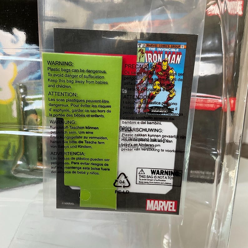May include: A clear plastic bag containing a Marvel Iron Man comic book cover. The cover features Iron Man in a red and gold suit. Warning labels in multiple languages are visible.