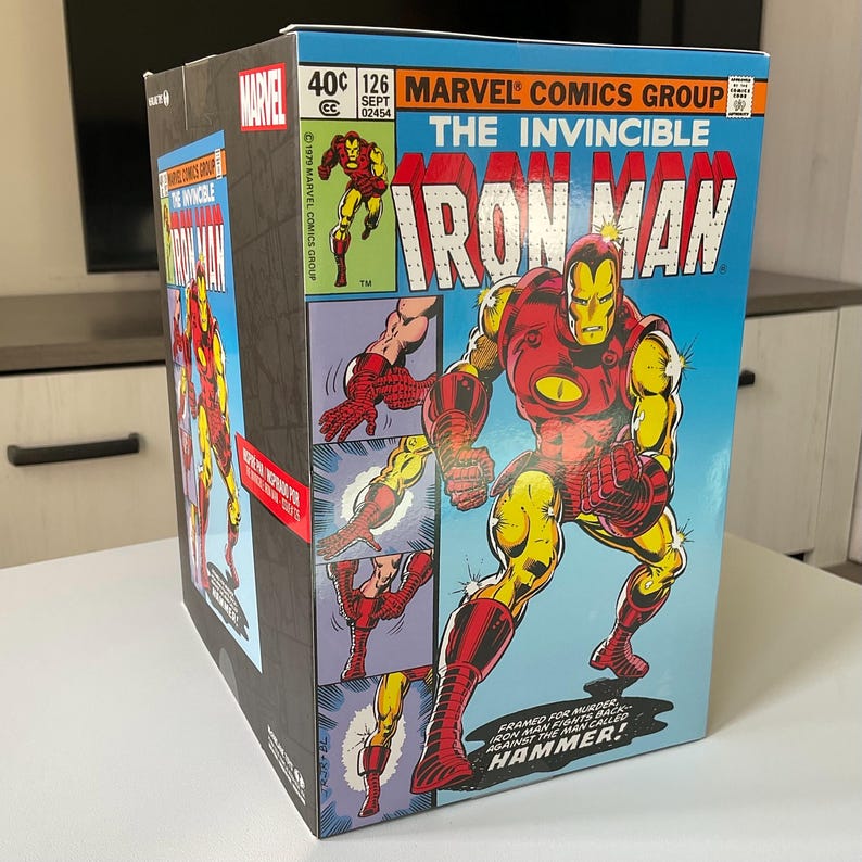 May include: A Marvel Comics Iron Man box featuring a comic book cover design. The cover art depicts Iron Man in a red and gold suit against a blue background. Text includes "The Invincible Iron Man" and "Marvel Comics Group."
