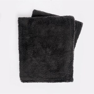 May include: A soft, dark gray throw blanket made of plush fabric. The blanket is folded in half and appears to be very cozy.