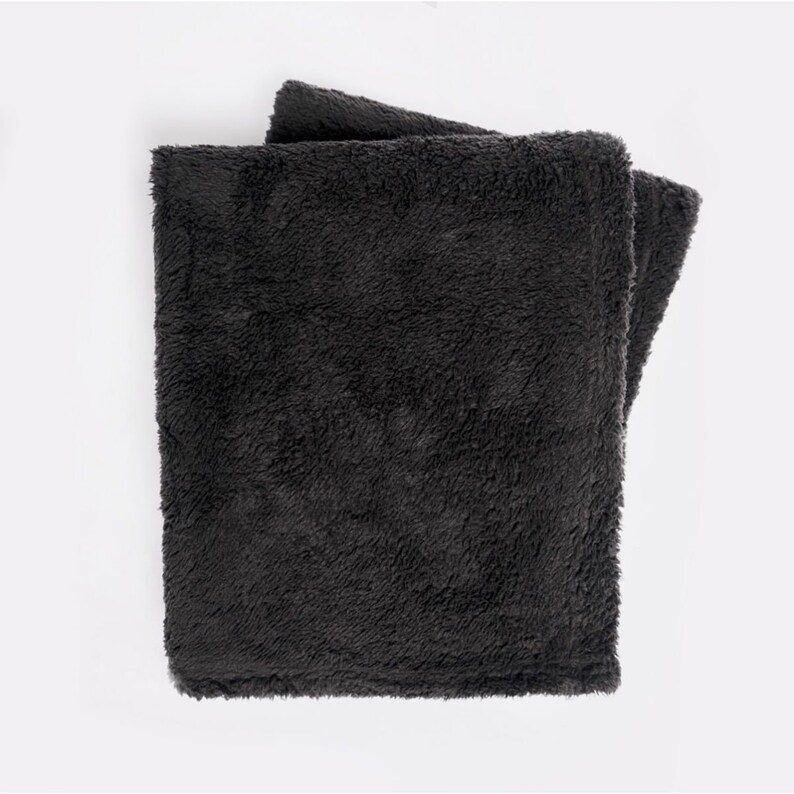 May include: A soft, dark gray throw blanket made of plush fabric. The blanket is folded in half and appears to be very cozy.