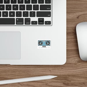 May include: A rectangular sticker featuring a light blue ultrasonic distance sensor with a grumpy face, two large eyes, and the text "I need 400cm of personal space." The sensor has four black pins extending from the bottom edge of the sticker design.