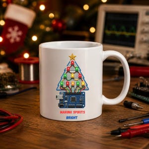 May include: A white ceramic mug featuring a graphic of a Christmas tree constructed from a breadboard, colorful LED lights, and a microcontroller board. The text below the graphic reads "MAKING SPIRITS BRIGHT" in red and blue capital letters.