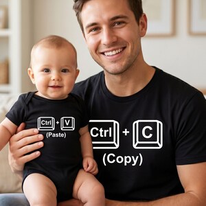 Könnte beinhalten: Ein schwarzer Baby-Body mit dem Text "Ctrl + V (Paste)" und ein schwarzes T-Shirt mit dem Text "Ctrl + C (Copy)". Das Baby trägt den Body und der Erwachsene das T-Shirt.