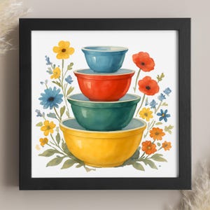 May include: A framed watercolor print featuring a stack of four colorful mixing bowls in blue, red, green, and yellow. The bowls are surrounded by watercolor flowers in various colors, including yellow, blue, and red.